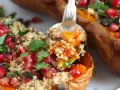 En sked tar en portion av ett läckert quinoa recept fyllt med pumpa, granatäpple och örter, serverat i en ugnsbakad butternut squash.