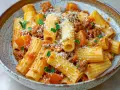 En skål med rigatoni pasta med en mustig köttfärssås och bitar av tomat. Toppad med riven parmesan och färsk persilja. Perfekt vin till salsiccia pasta.