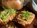 Två rostade brödskivor med krämigt refried beans, toppade med groddar och frön. En burk med pålägget syns i bakgrunden.