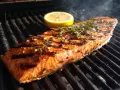 En saftig grillad laxsida med örter och en citronskiva på grillen. Röken stiger och doften sprider sig.