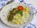 En tallrik med panerad fisk, dillstuvad potatis, en tomatklyfta och en citronklyfta. Allt serveras på en tallrik med blått mönster.