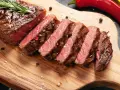 Perfekt stekt entrecote, skivad och serverad med rosmarin, pepparkorn och flingsalt på en träskärbräda. En röd chili ligger bredvid.