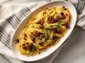 En skål med spaghetti, toppad med soltorkade tomater, svarta oliver och färsk persilja. En härlig pasta puttanesca!