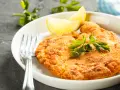 En gyllene schnitzel med citronklyfta och persilja, redo att avnjutas med ett glas vin till schnitzel.