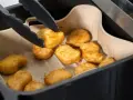 Tång tar upp gyllene, krispiga tater tots ur en airfryer.