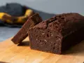 Chokladig banankaka, perfekt för ett enkelt banankaka recept. En skiva är uppskuren och en övermogen banan ligger i bakgrunden.