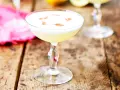En krämig pisco sour med ett vitt skum och en touch av kanel på en rustik träyta.