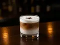En krämig White Russian med kaffebönor på toppen, serverad i ett glas på en mörk träyta.