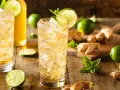 En uppfriskande ginger beer drink med is, lime och mynta. Ingredienser som ingefära och lime ligger utspridda.