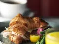 En gyllene croissant fylld med skinka och ost, serverad med grönsaker och juice. Perfekt för en snabb frukost eller lunch, som ett enkelt croissant recept.