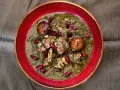 En skål med ghorme sabzi, en mustig persisk gryta med kött, örter och röda bönor, serverad i en röd kantad skål.
