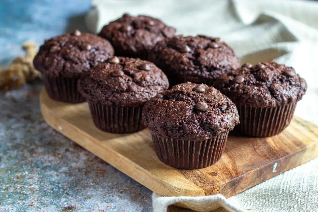 Fem saftiga chokladmuffins med chokladknappar på en träbricka. Perfekt för ett chokladmuffins recept.