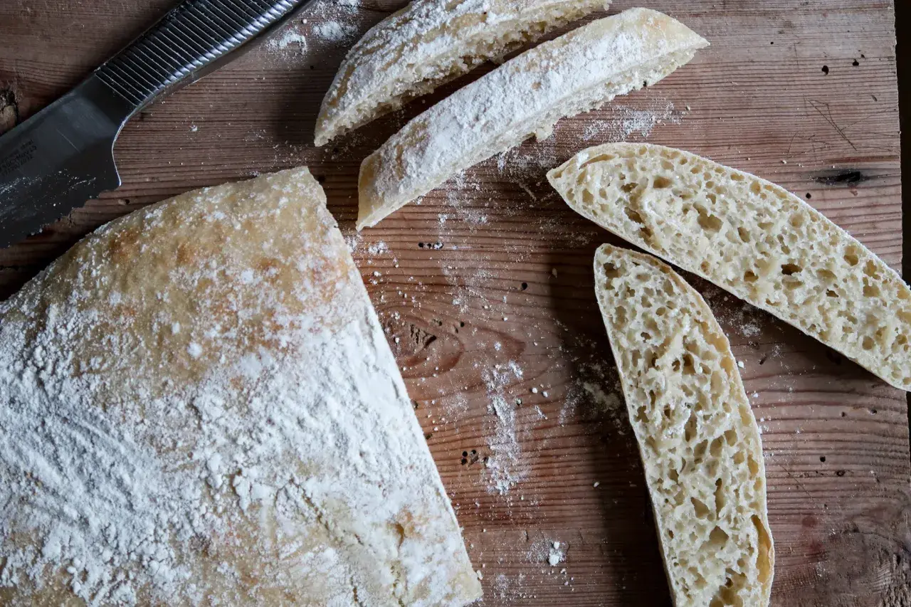 En hel och skivad ciabatta på en träskärbräda, redo för ett gott ciabatta recept. Mjöl strött över.