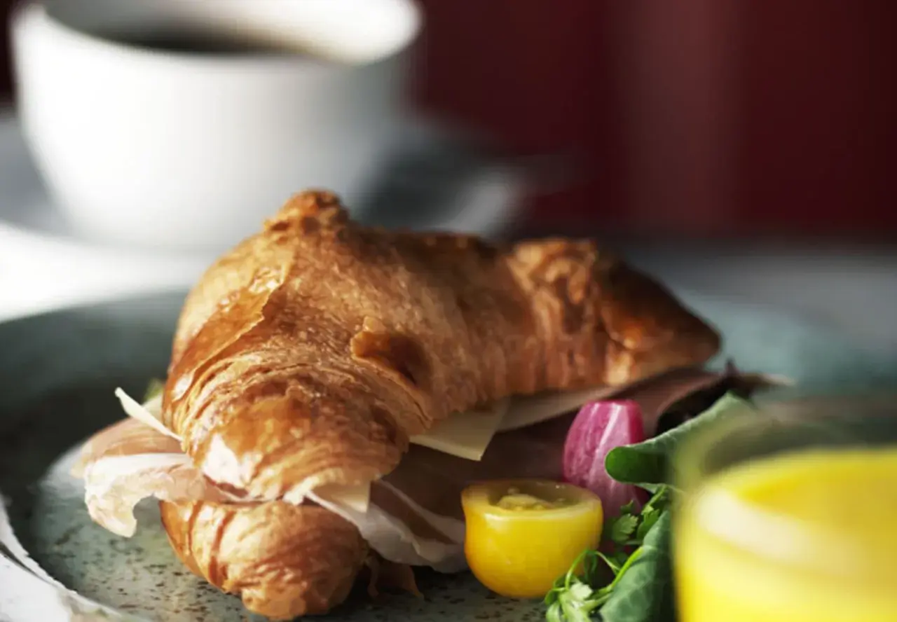 En gyllene croissant fylld med skinka och ost, serverad med grönsaker och juice. Perfekt för en snabb frukost eller lunch, som ett enkelt croissant recept.