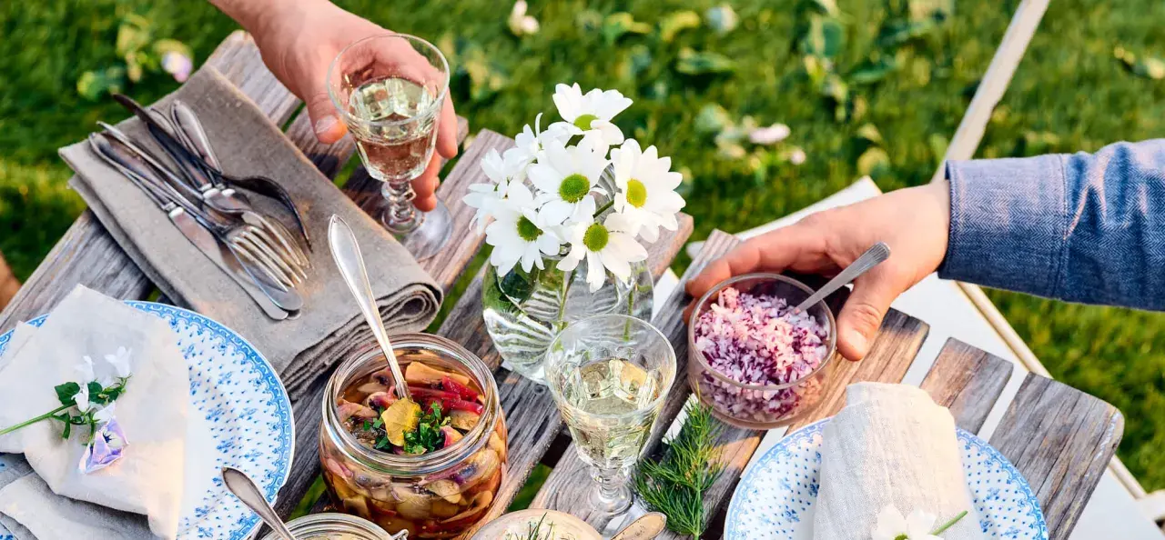 En härlig sommarmåltid med inlagd sill, hackad rödlök och vitt vin till sillen. Blommor och grönska i bakgrunden.