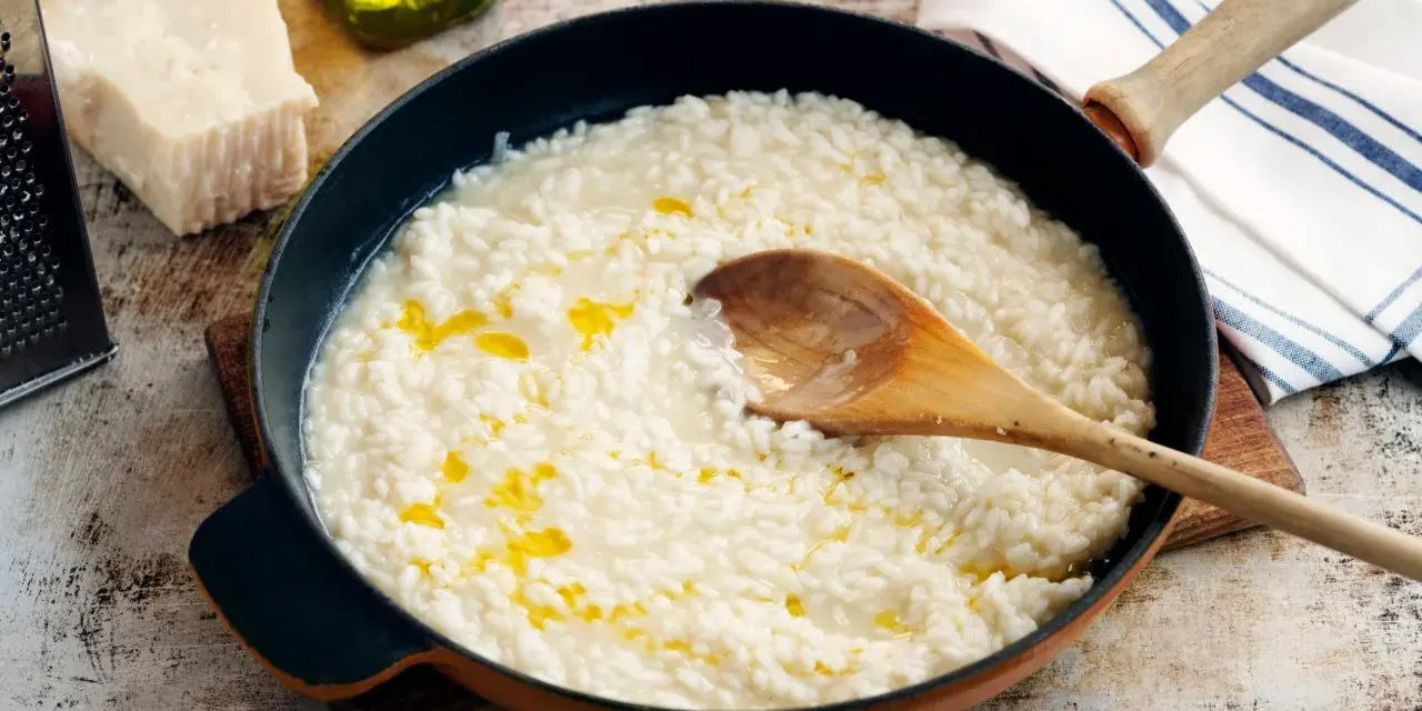Krämig risotto i panna, med parmesan, olivolja och en träsked. Perfekt för ett enkelt risotto recept.