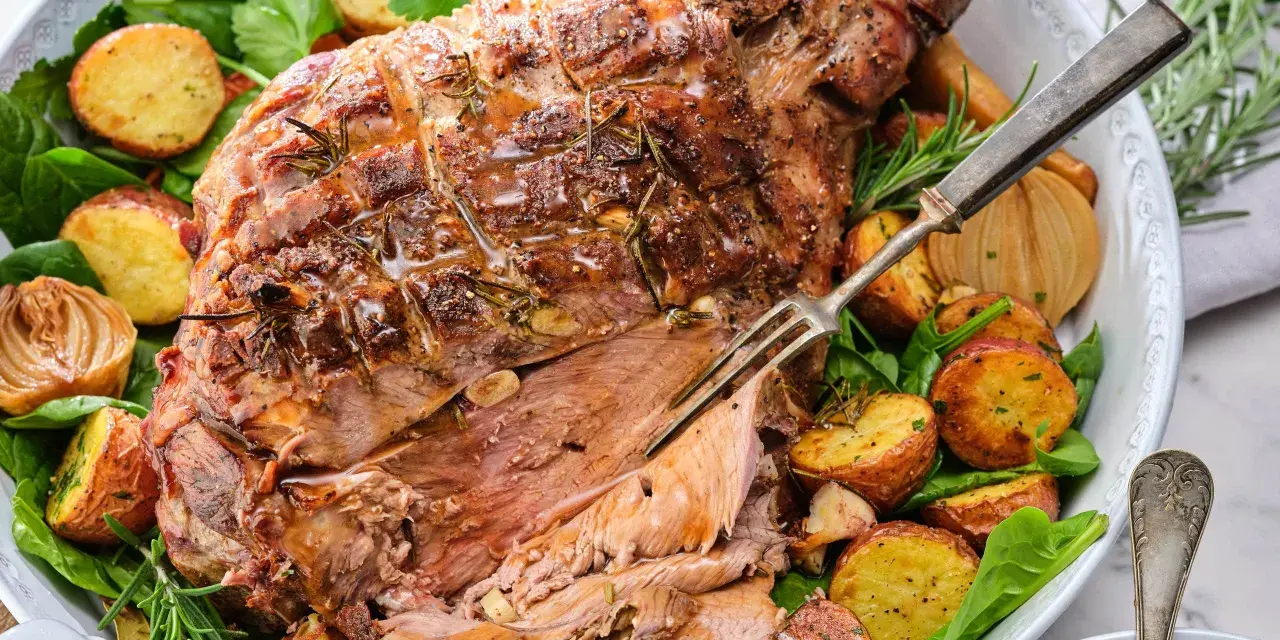 En saftig lammstek med ben, omgiven av rostade potatisar, lök och färska örter. Perfekt för en festlig middag.