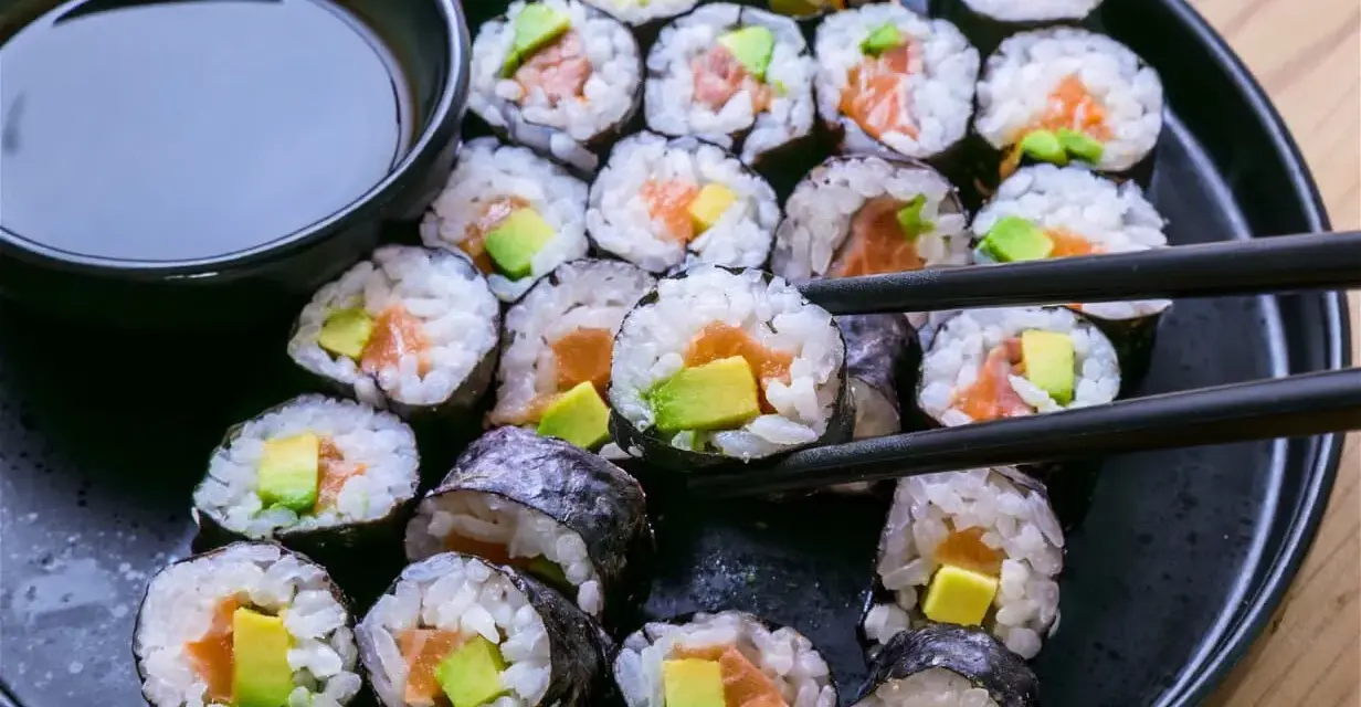 En tallrik med hemgjord sushi, perfekt för ett enkelt sushi recept. Lax och avokado rullade i ris och nori, med en skål sojasås.