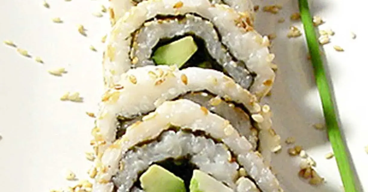 En närbild på en california roll med sesamfrön och en grön garnityr.