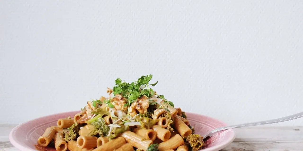 En läcker vegetarisk pasta med broccoli, valnötter och färska örter på en rosa tallrik.
