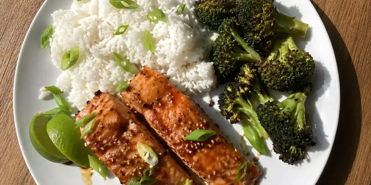 Två saftiga filéer av asiatisk lax serveras med fluffigt ris, rostad broccoli och limeklyftor.