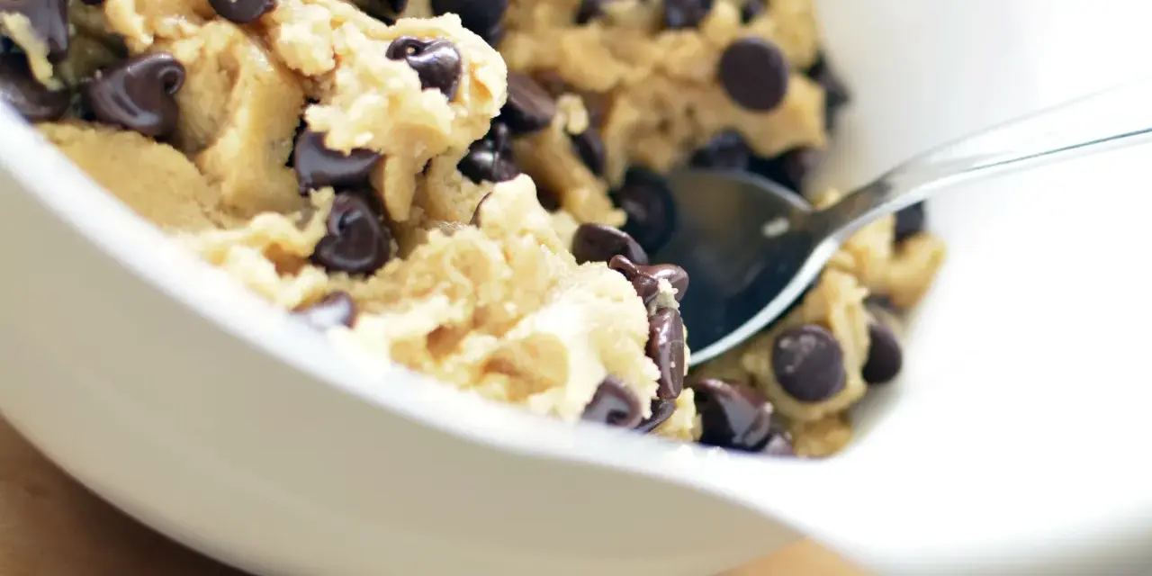 En skål med ljuvlig cookie dough med chokladbitar, redo för ett enkelt cookie dough recept. En sked vilar i smeten.