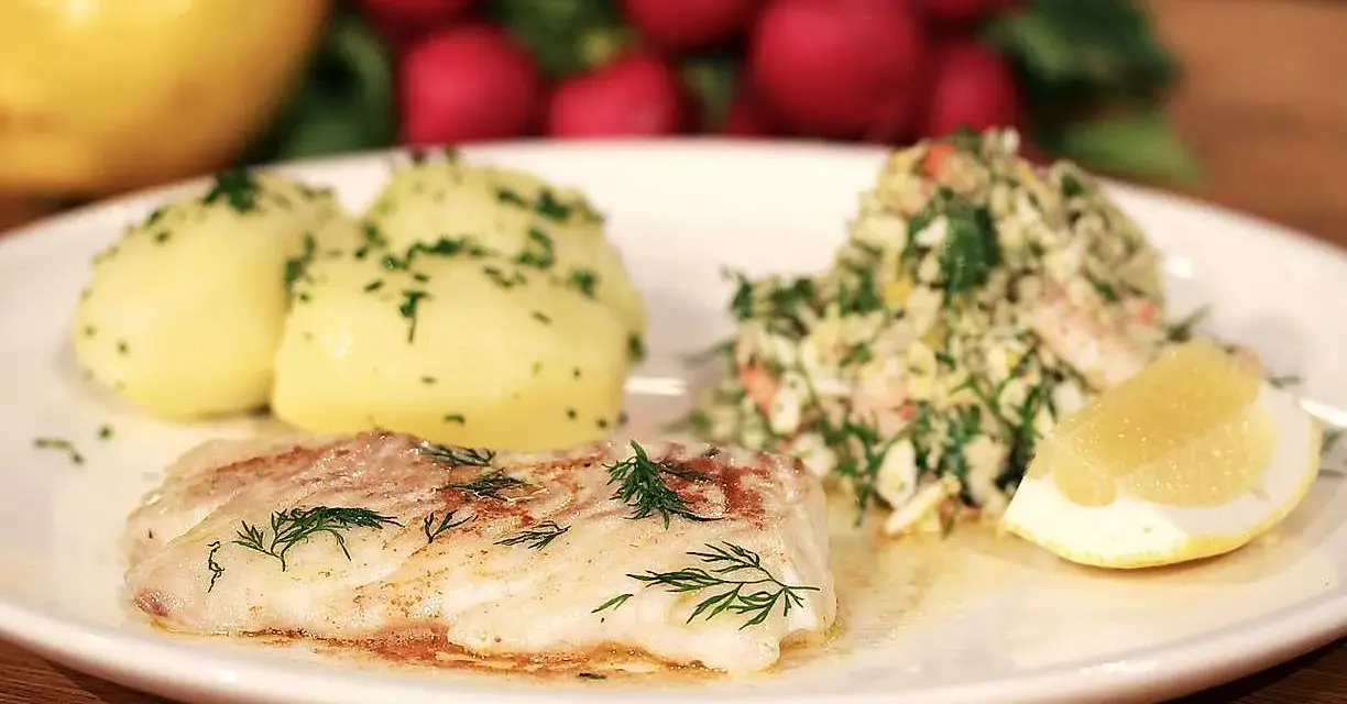 En tallrik med stekt kolja, dill, potatis och en citronskiva. Ett perfekt kolja recept för en god middag.