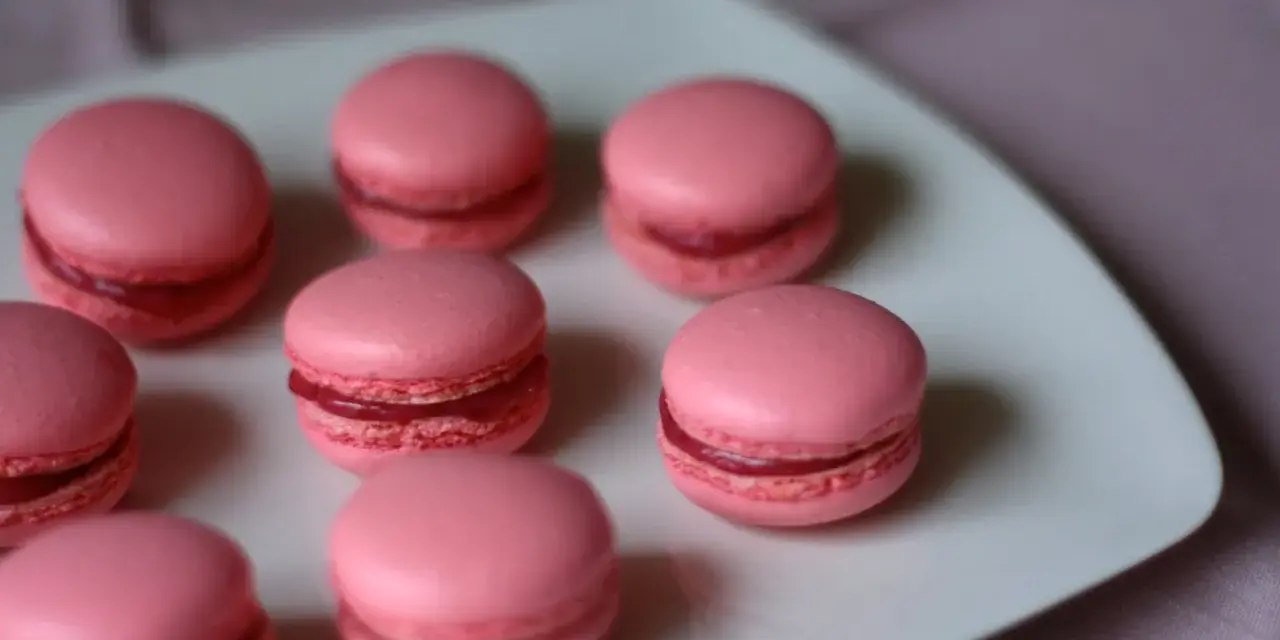 Rosa macarons med hallonfyllning på en vit tallrik. Perfekt för ett macarons recept.
