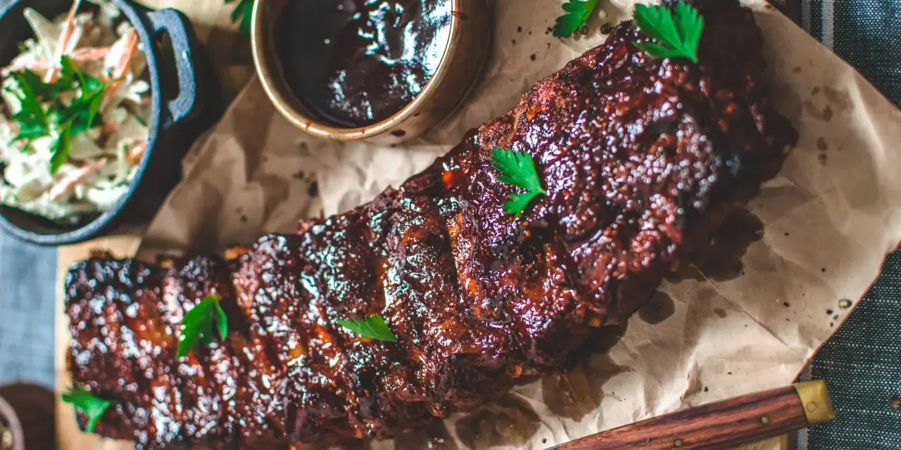 Saftiga spareribs i ugn, glaserade och serverade med en skål coleslaw och BBQ-sås. Perfekt för en festmåltid!