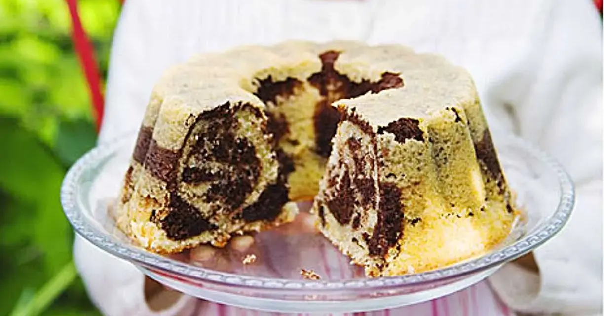 En barn håller upp en marmorerad tigerkaka på ett fat. Ett perfekt tigerkaka recept för fikat.