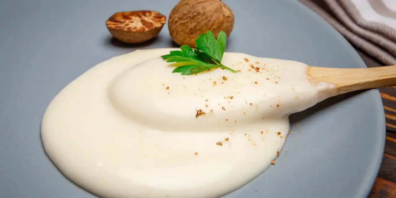 Krämig bechamelsås på en tallrik med muskotnötter och persilja. Ett perfekt bechamelsås recept för alla tillfällen.