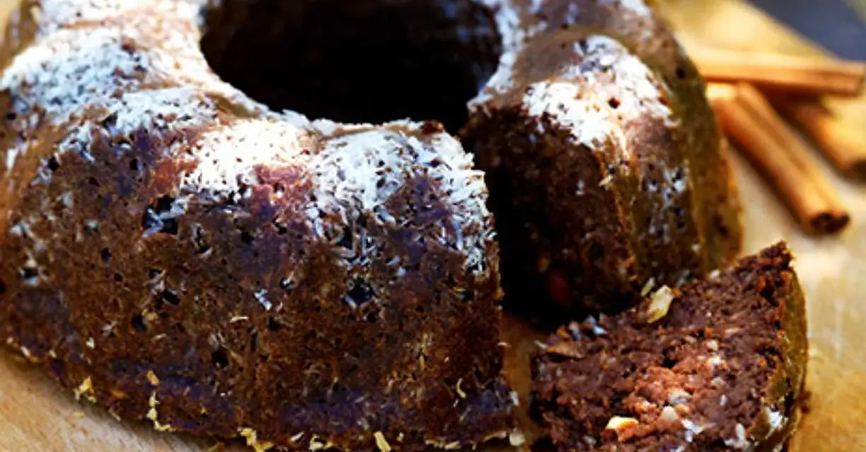 En saftig banankaka med choklad, toppad med kokosflingor. En bit är uppskuren och visar den rika, mörka insidan.