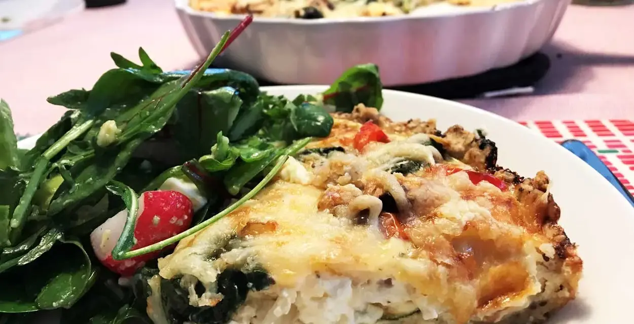 En bit krämig vegetarisk paj med ost och grönsaker, serverad med en fräsch sallad.