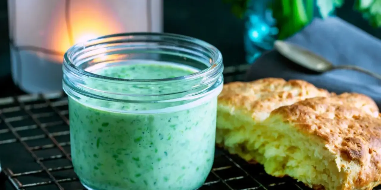 En burk med krämig, grön dressing, perfekt för ett grönt gudinnedressing recept. Bredvid ligger nybakade scones.