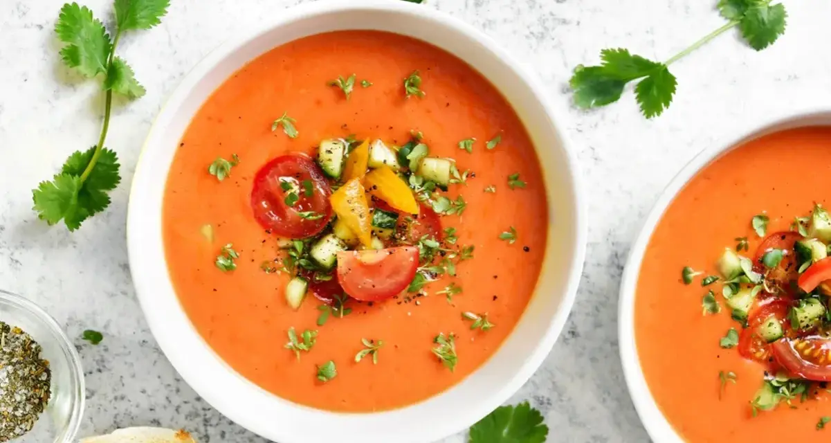 Två skålar med uppfriskande gazpacho, toppad med färska grönsaker. Ett perfekt gazpacho recept för varma dagar.