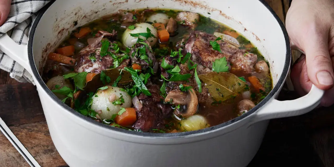 En gryta med mustig coq au vin, fylld med möra kycklingbitar, champinjoner, lök och morötter, toppad med färsk persilja.