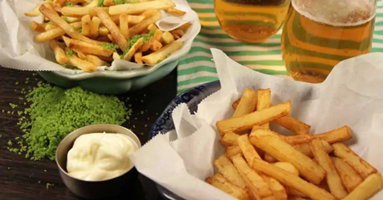 Två skålar med krispiga pommes frites, en med grön kryddning, bredvid två glas öl och en skål majonnäs.