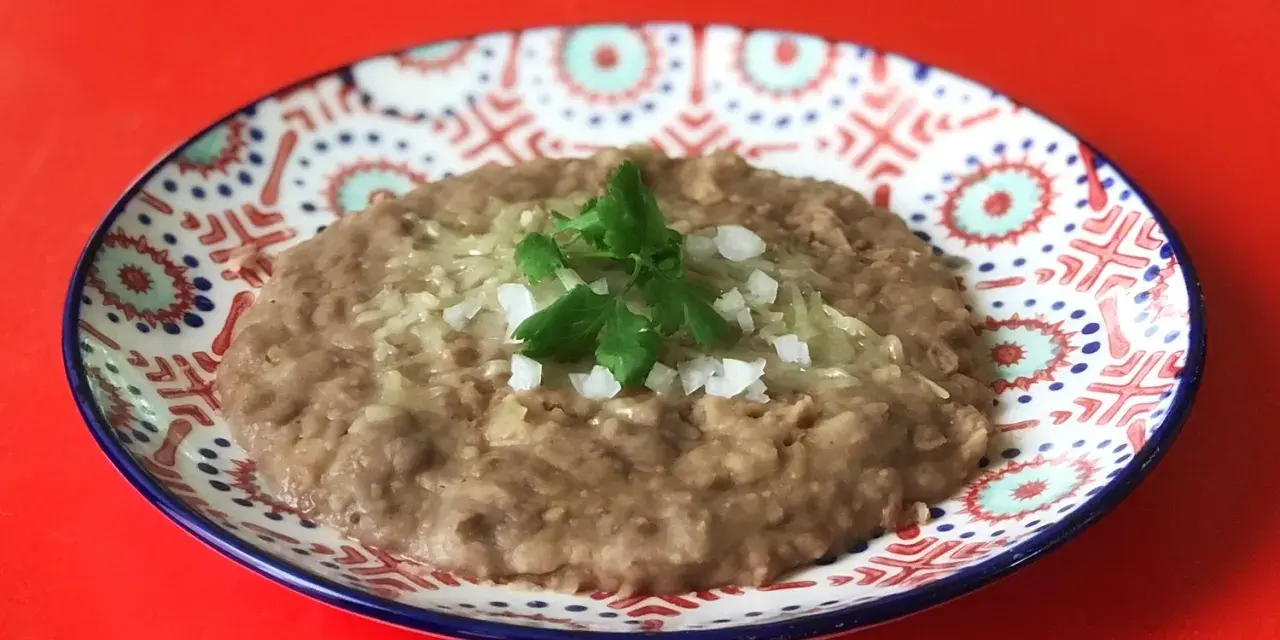 En tallrik med refried beans, toppad med lök och persilja. Ett enkelt och gott refried beans recept.