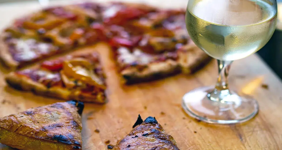 En skiva pizza med ett glas vitt vin. Perfekt vin till pizza för en mysig kväll.