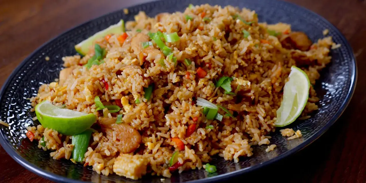 En tallrik med utsökt fried rice, garnerad med limeklyftor och salladslök.