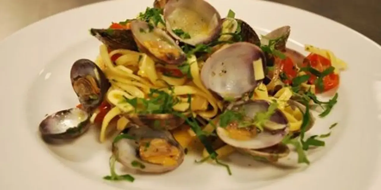 En tallrik med pasta vongole, där färska vongole-musslor blandas med tagliatelle, körsbärstomater och persilja.