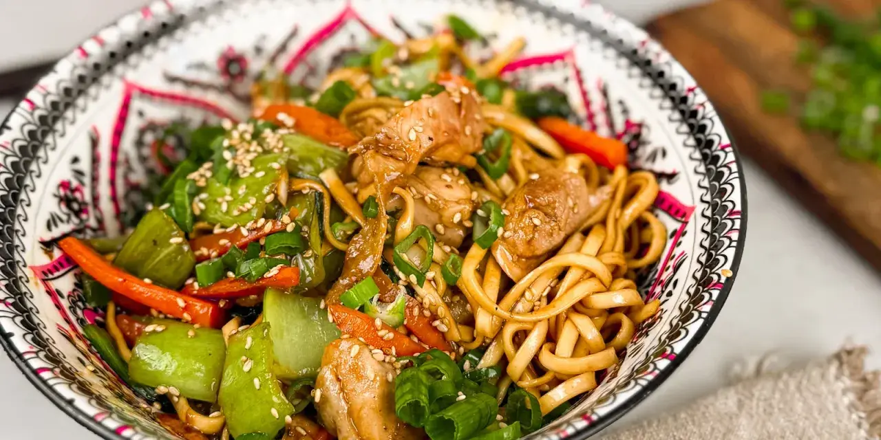En skål med kycklingwok med nudlar, grönsaker och sesamfrön. En härlig och färgstark måltid.