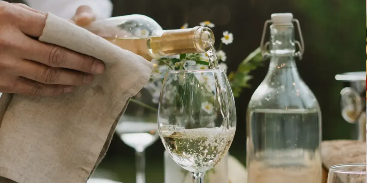 En hand häller upp vitt vin i ett glas. Den perfekta vitt vin temperatur är avgörande för smaken.