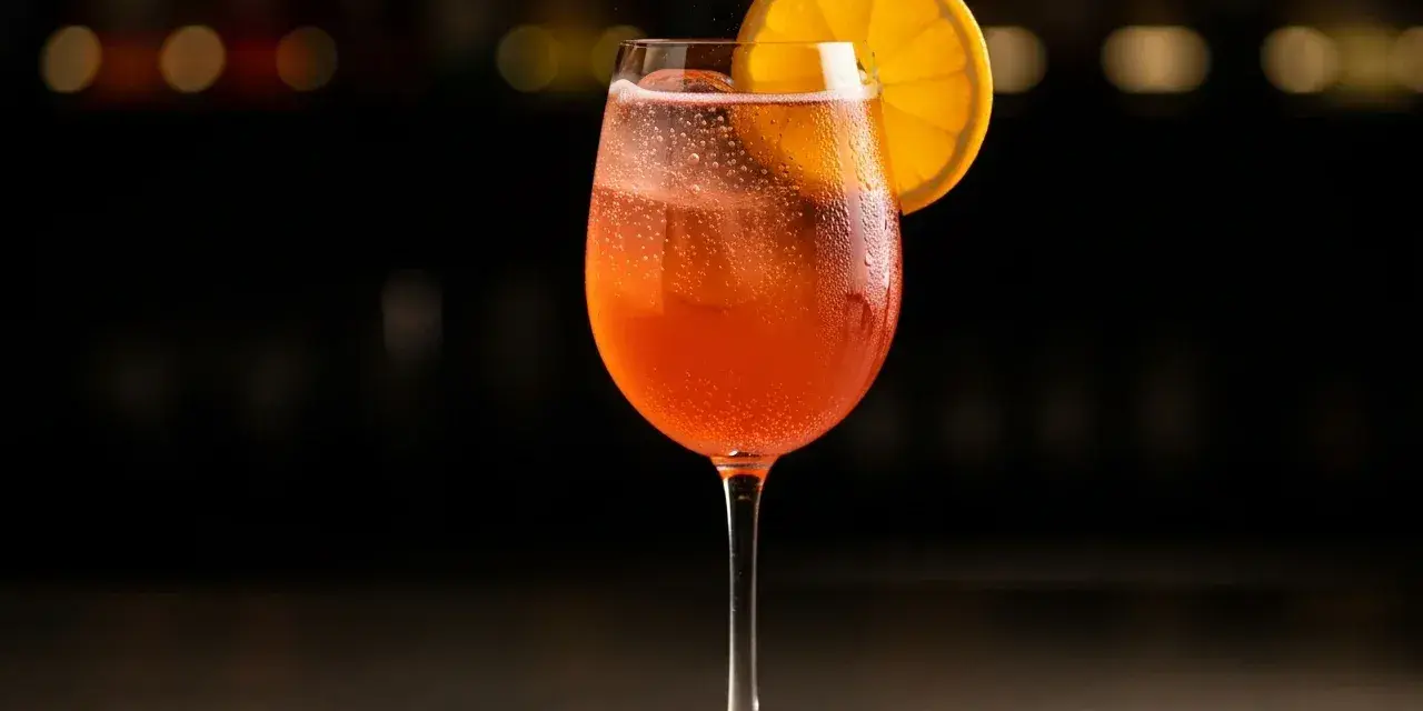 Ett glas med bubblig, orange drink, troligen en cava aperol, med en apelsinskiva som garnering.