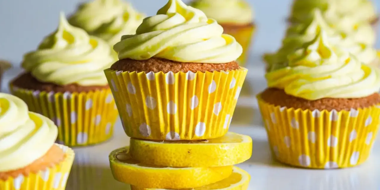 Gula citronmuffins med fluffig frosting, serverade i prickiga formar. Perfekt för ett citronmuffins recept!