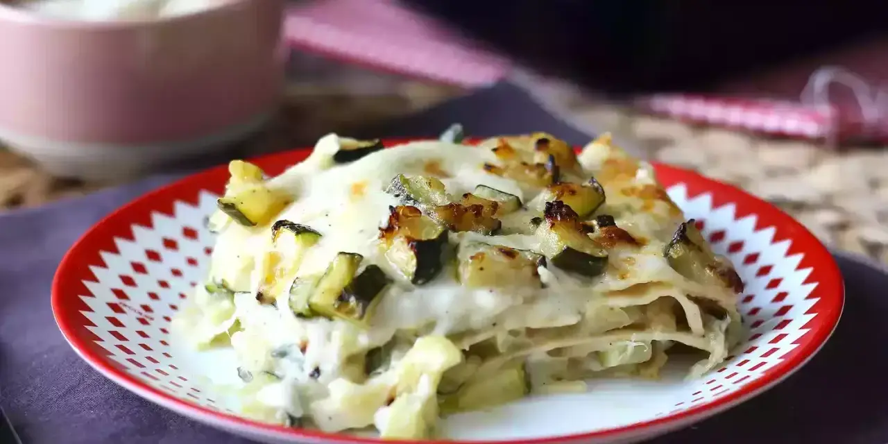 En bit krämig vegetarisk lasagne med zucchini, toppad med gyllene ost och grönsaker.