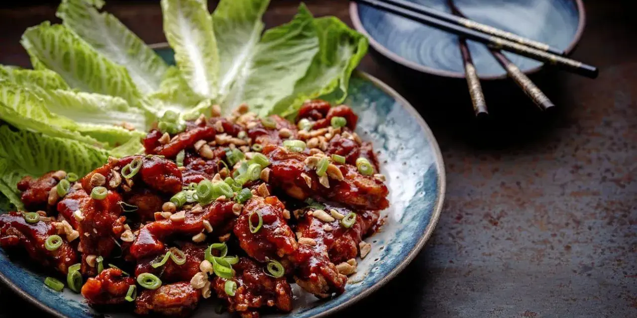 En tallrik med krispiga, glaserade kycklingvingar, toppade med hackade jordnötter och salladslök. Serveras med krispiga salladsblad. En utsökt koreansk matupplevelse.