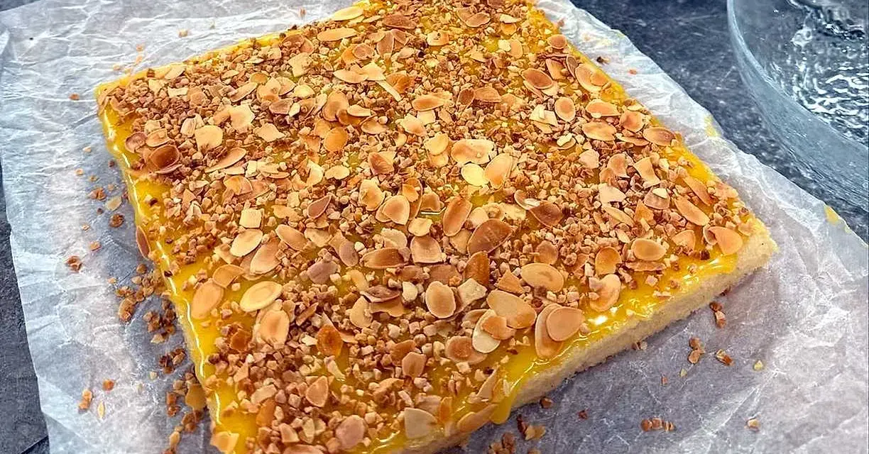 En fyrkantig silviakaka med gul glasyr och strössel av hackade nötter och mandel. Perfekt för ett fika-recept!