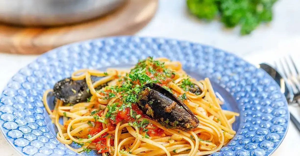 En tallrik med frutti di mare pasta, toppad med färsk persilja och serverad i en blåmönstrad skål.