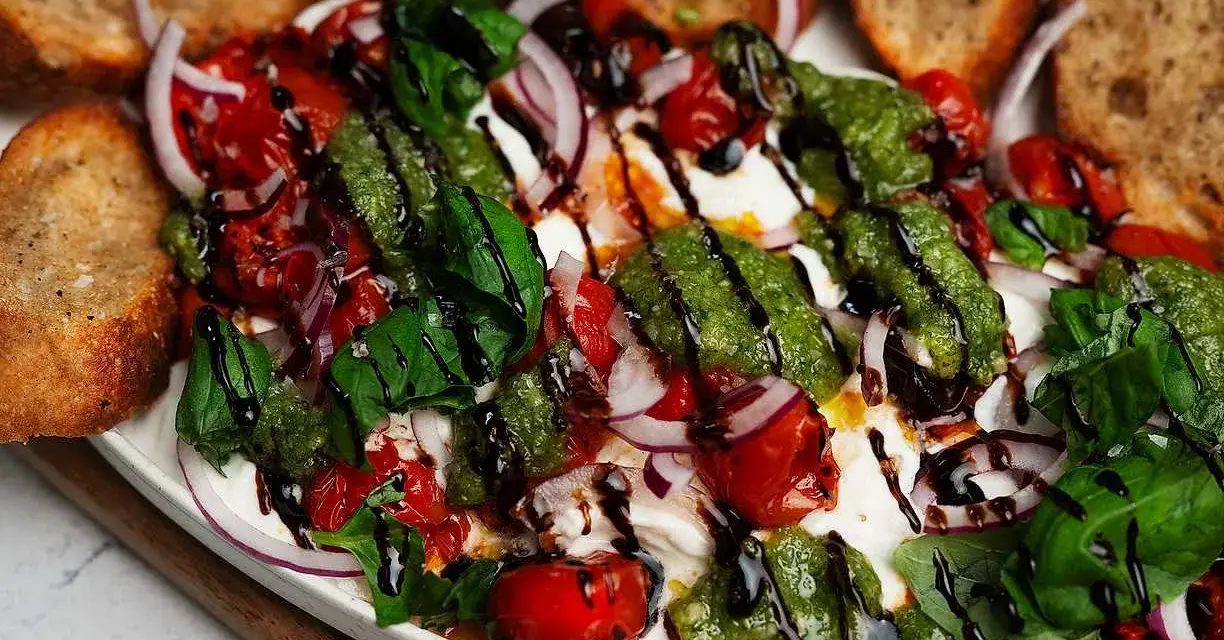 En krämig burrata med tomater, rödlök, basilika och pesto. Perfekt tillbehör till grillat bröd. Ett enkelt burrata recept.